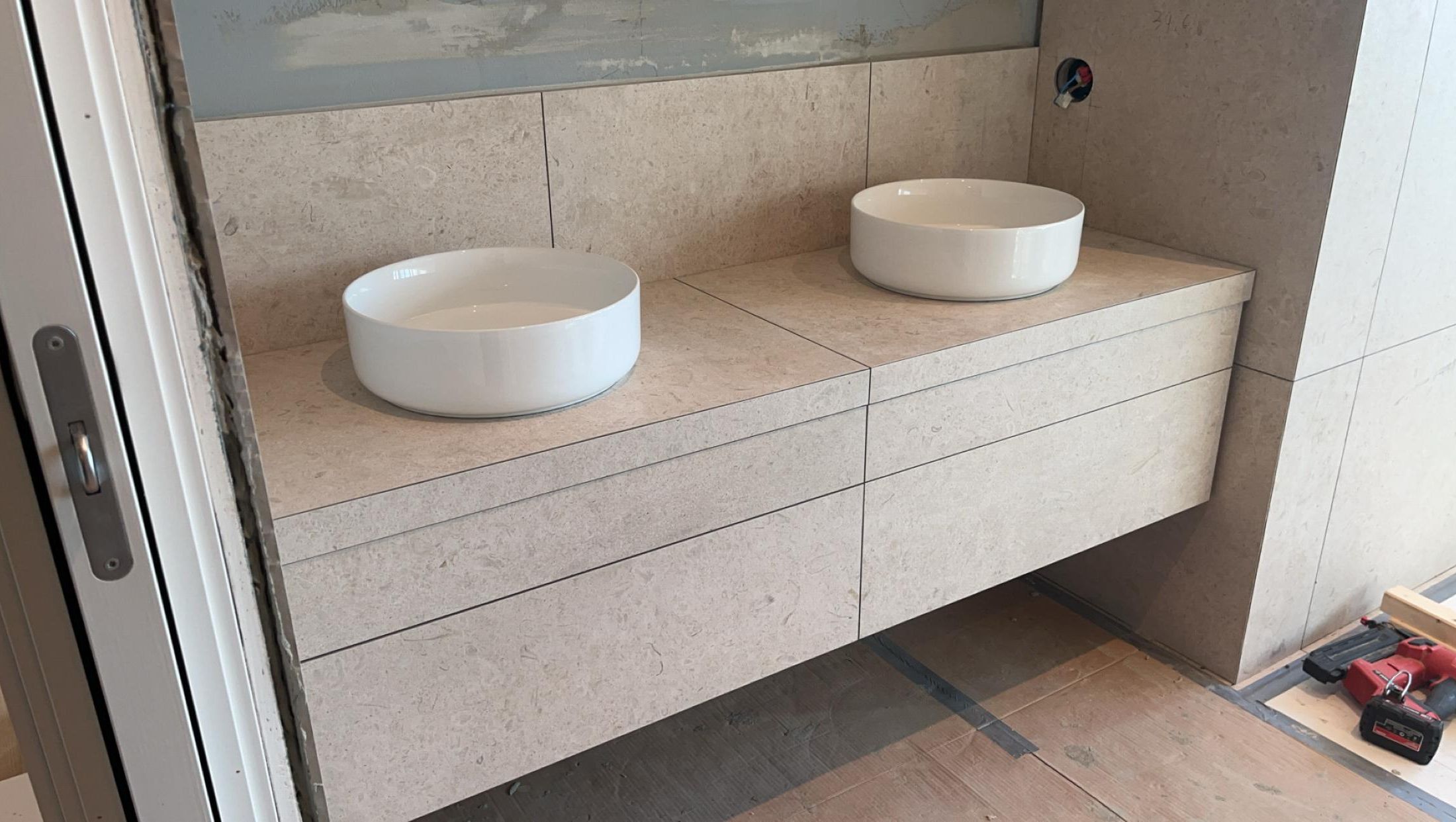 Dobbel servantløsning under montering med lyse fliser og to runde servanter på skuffefront i steinlook.