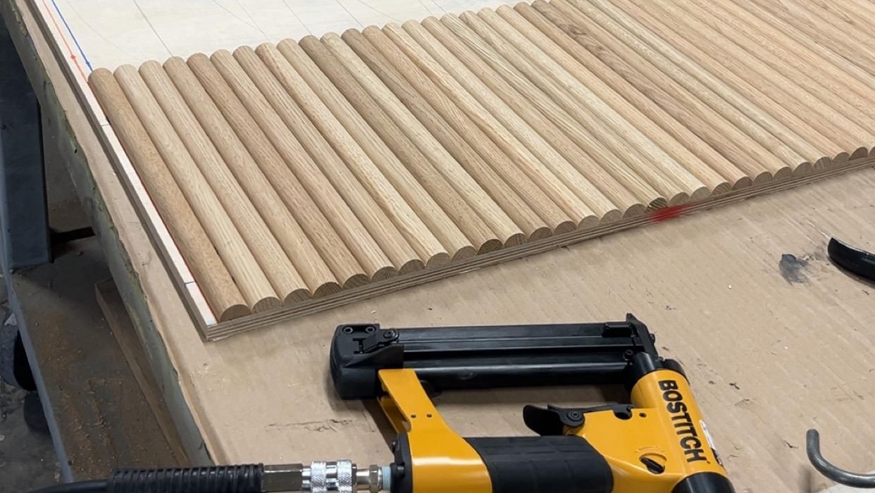 Halvsirkelformede tredeler ligger sortert på arbeidsbord, med en gul og svart spikerpistol foran.